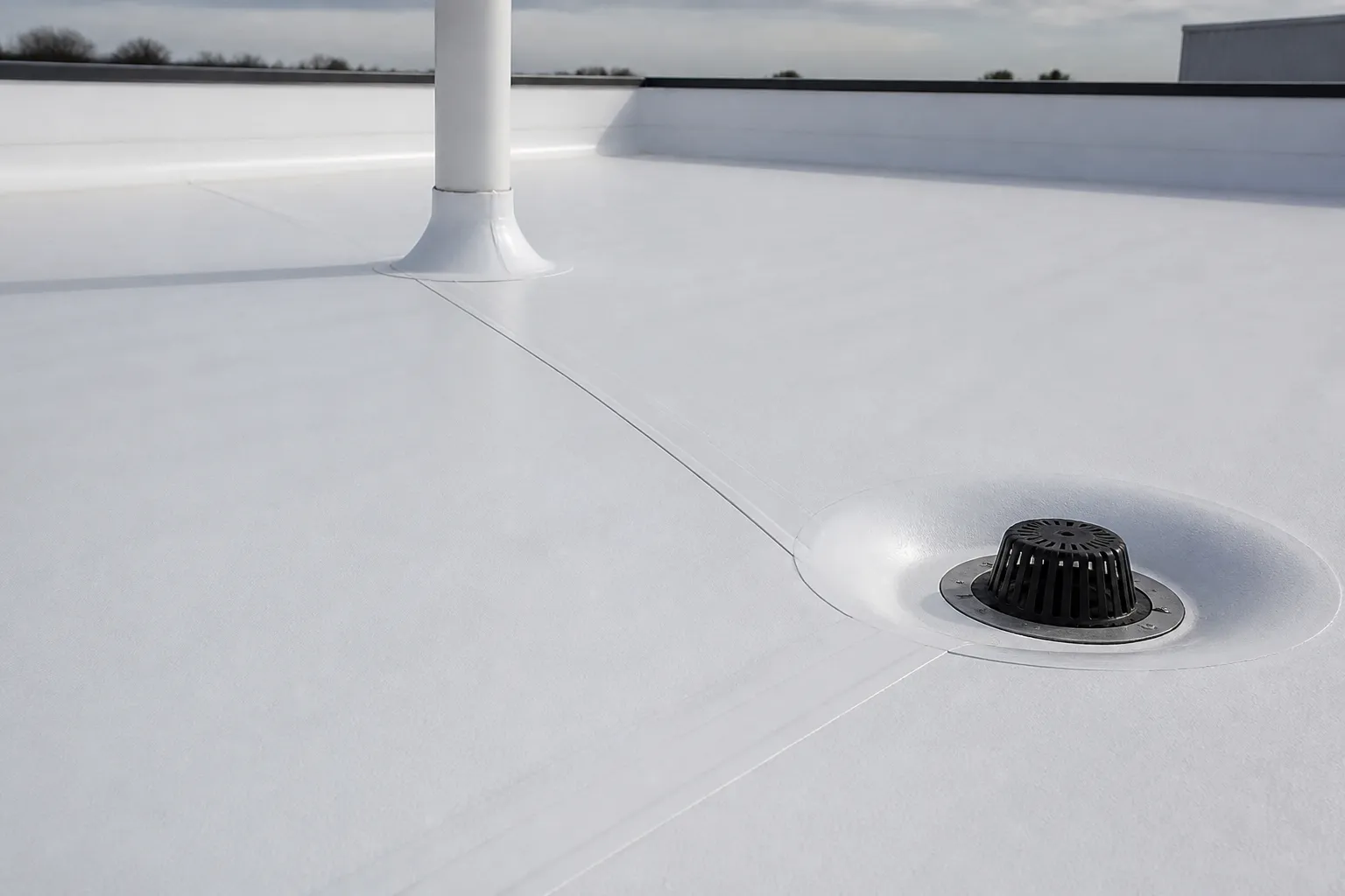 White commercial roof membrane seam beside a roof drain, with pipe-penetration flashing nearby