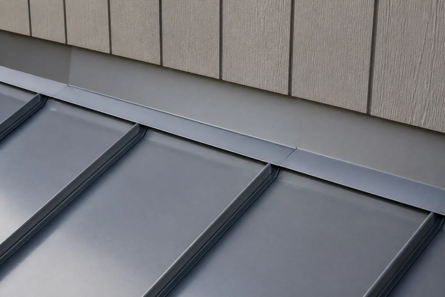 Raised standing-seam metal roof panels meeting formed flashing at a roof-to-wall transition