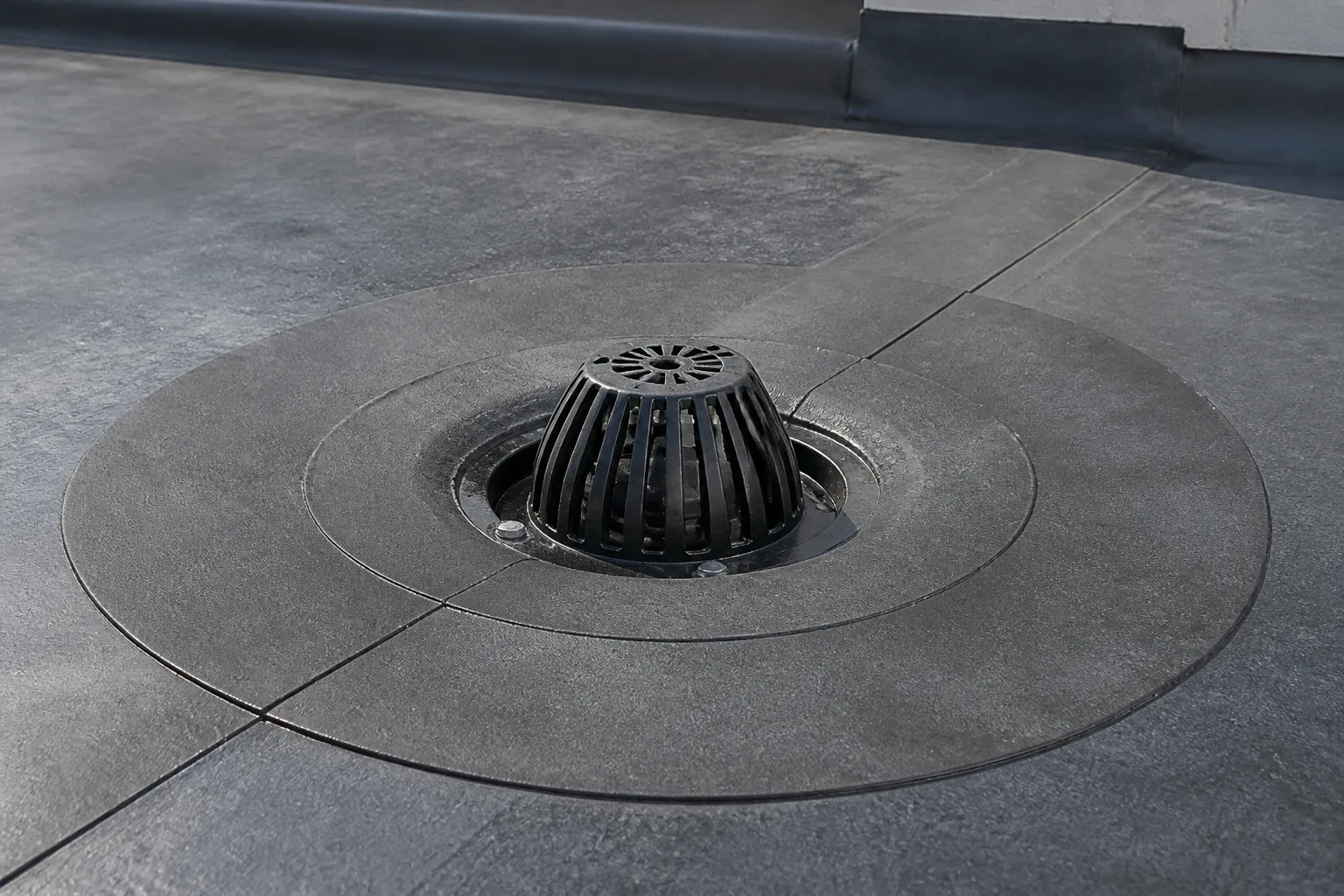 Commercial low-slope roof drain surrounded by membrane flashing and roof seams