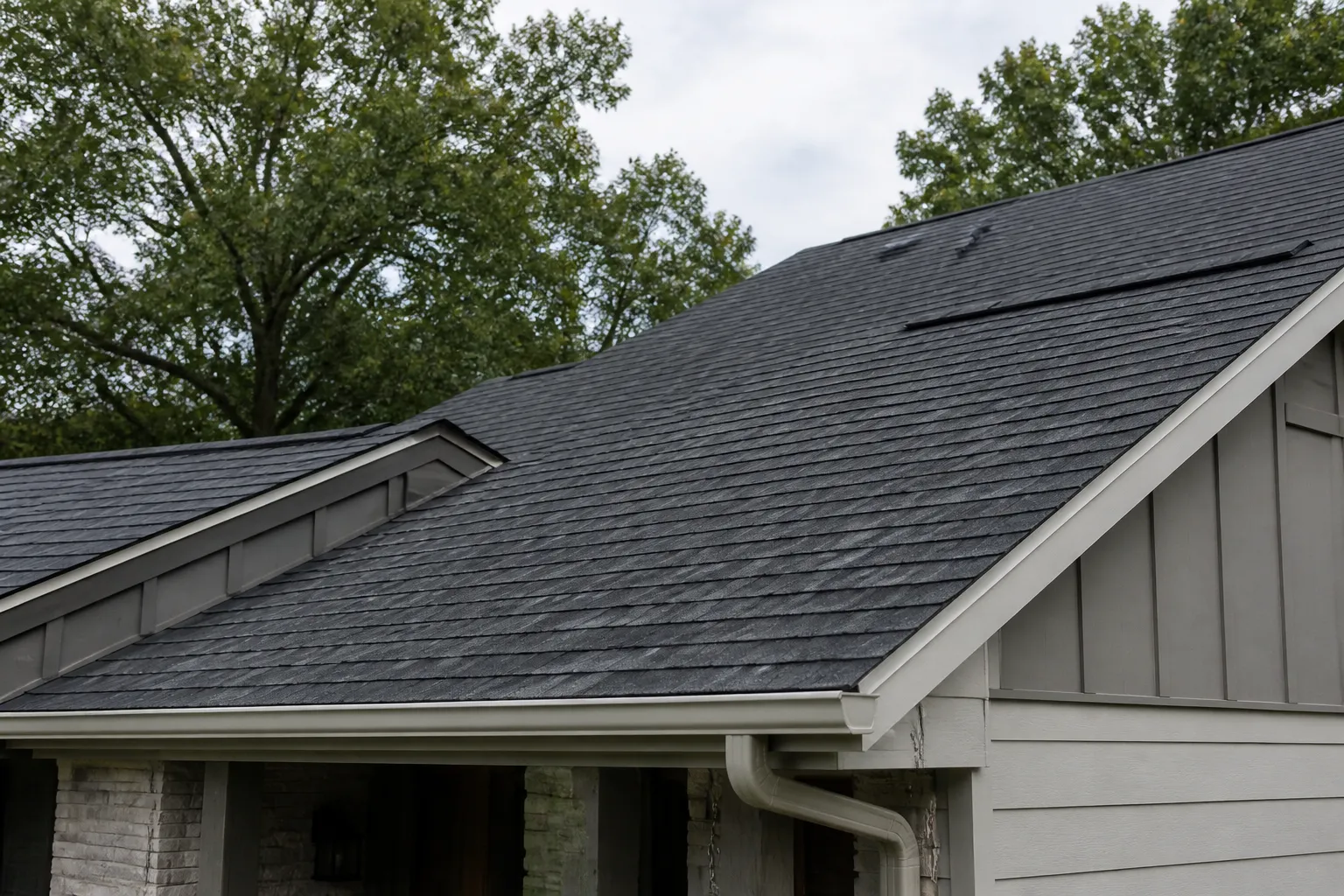 Charcoal asphalt-shingle roof with metal flashing on a home in daylight